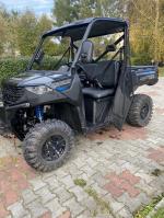 Dzień, quad Polaris Ranger stoi na drodze z kostki brukowej, w tle zieleń.