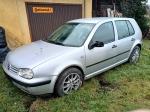 Srebrny Volkswagen Golf stoi na trawie, za nim budynek garażowy.